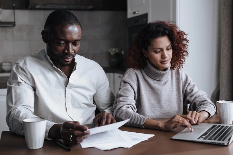 A couple sitting together at a table, looking at a laptop with charts and a calendar.